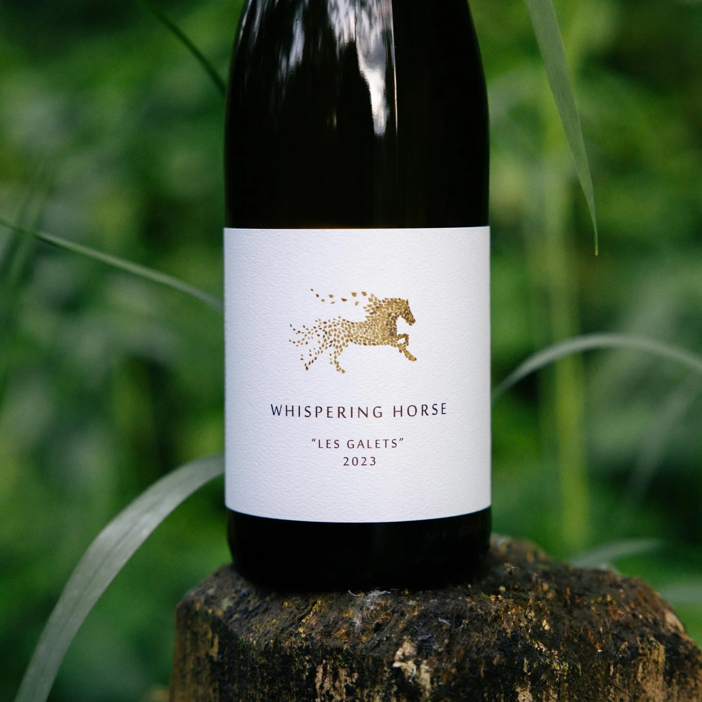 Wine bottle labeled 'Whispering Horse' on a wooden block with a green grass background