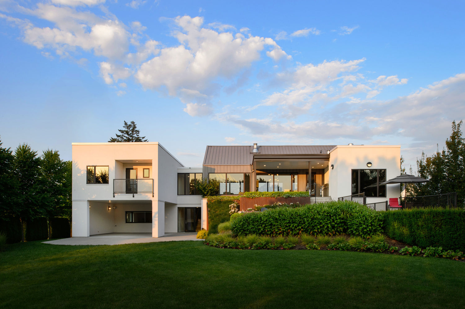 View of back of modern home at sunset, landscape design includes green grass, shrubs and grasses with corten steel elements. 